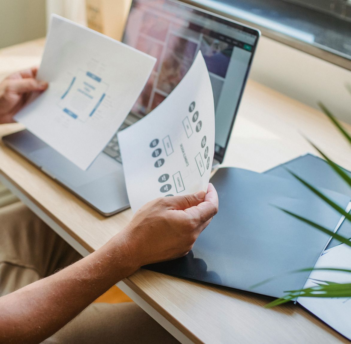 hands holding paper with charts viewing computer screen